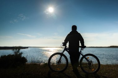 Yalnız bir adam bisiklet'nde günbatımı rahatlatıcı ile gökyüzü deniz, nehir