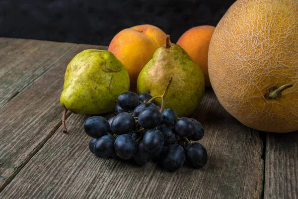 Melão, uvas, pêssego e pêra na velha mesa de madeira . — Fotografia de Stock