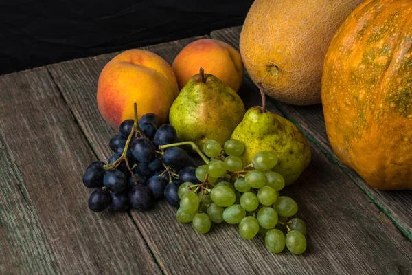 Melão, uvas, pêssego, pêra e abóbora na velha mesa de madeira . — Fotografia de Stock