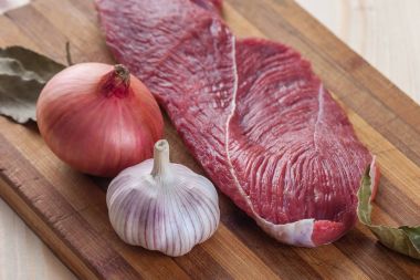 Et, defne yaprağı, sarımsak ve soğan bir kesme tahtası üzerinde