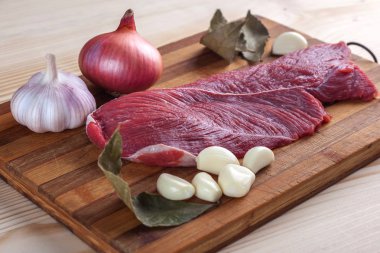 Et, defne yaprağı, sarımsak ve soğan bir kesme tahtası üzerinde