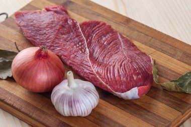 Et, defne yaprağı, sarımsak ve soğan bir kesme tahtası üzerinde
