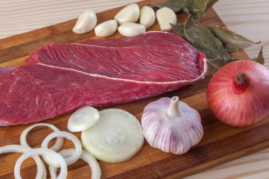 Et, defne yaprağı, sarımsak ve soğan bir kesme tahtası üzerinde