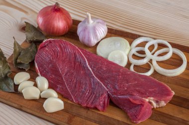 Et, defne yaprağı, sarımsak ve soğan bir kesme tahtası üzerinde