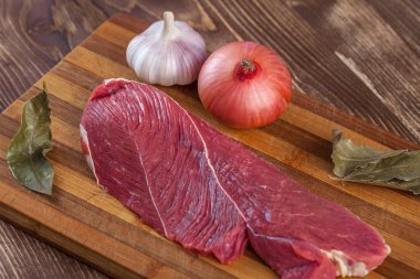 Et, defne yaprağı, sarımsak ve soğan bir kesme tahtası üzerinde