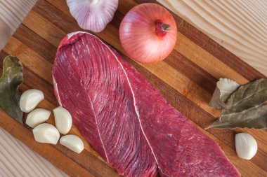 Et, defne yaprağı, sarımsak ve soğan bir kesme tahtası üzerinde