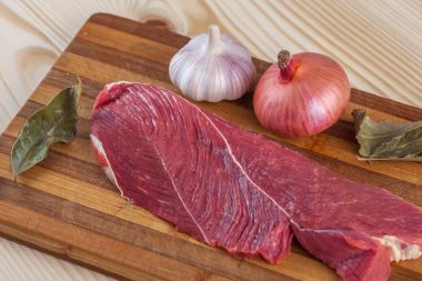 Et, defne yaprağı, sarımsak ve soğan bir kesme tahtası üzerinde