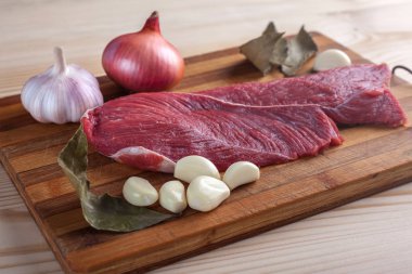 Et, defne yaprağı, sarımsak ve soğan bir kesme tahtası üzerinde