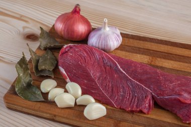 Et, defne yaprağı, sarımsak ve soğan bir kesme tahtası üzerinde