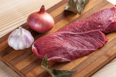 Et, defne yaprağı, sarımsak ve soğan bir kesme tahtası üzerinde