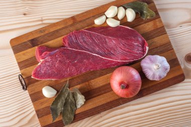 Et, defne yaprağı, sarımsak ve soğan bir kesme tahtası üzerinde