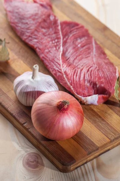 Et, defne yaprağı, sarımsak ve soğan bir kesme tahtası üzerinde