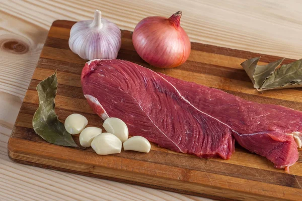 Et, defne yaprağı, sarımsak ve soğan bir kesme tahtası üzerinde