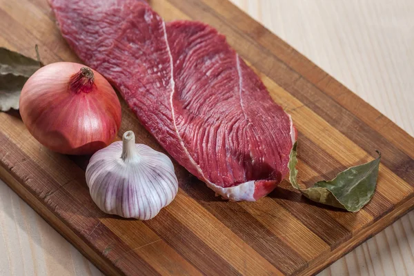 Et, defne yaprağı, sarımsak ve soğan bir kesme tahtası üzerinde