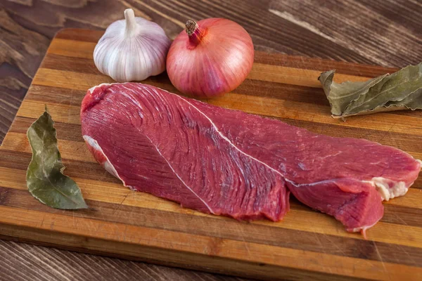 Et, defne yaprağı, sarımsak ve soğan bir kesme tahtası üzerinde