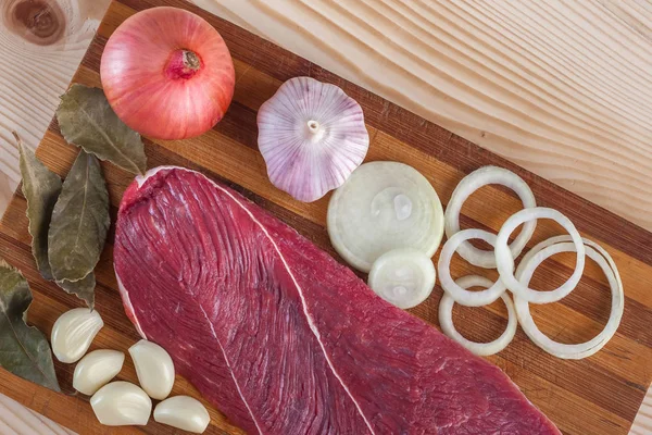 Et, defne yaprağı, sarımsak ve soğan bir kesme tahtası üzerinde