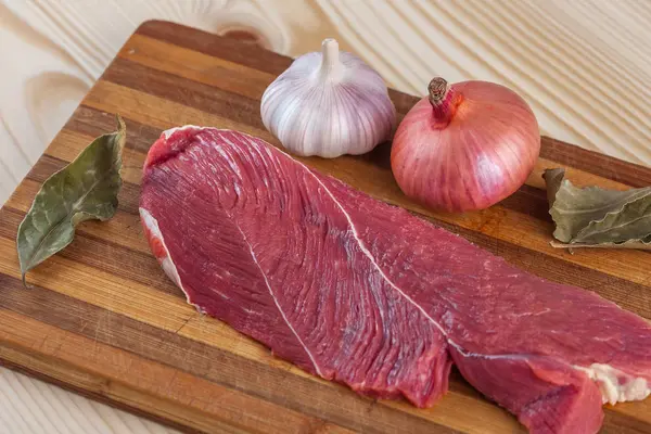 Et, defne yaprağı, sarımsak ve soğan bir kesme tahtası üzerinde
