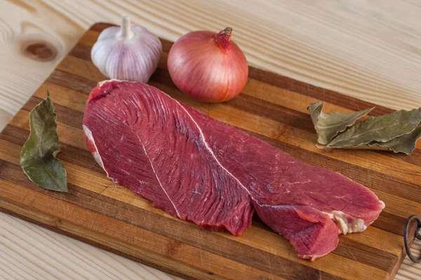 Et, defne yaprağı, sarımsak ve soğan bir kesme tahtası üzerinde