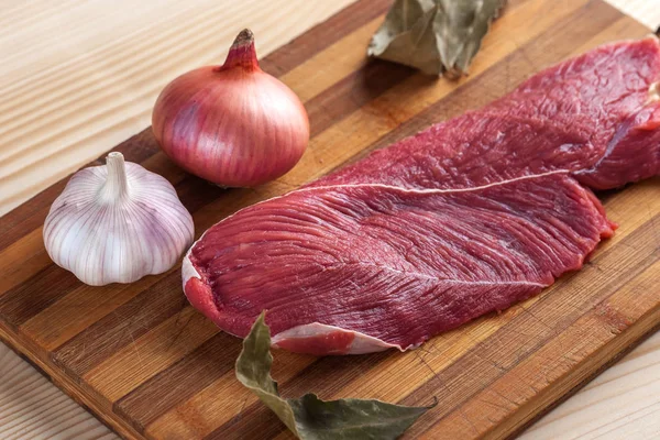 Et, defne yaprağı, sarımsak ve soğan bir kesme tahtası üzerinde