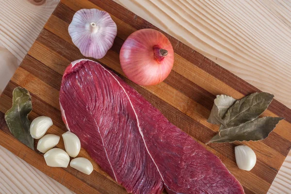 Et, defne yaprağı, sarımsak ve soğan bir kesme tahtası üzerinde
