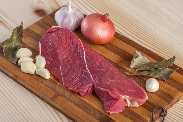 Et, defne yaprağı, sarımsak ve soğan bir kesme tahtası üzerinde