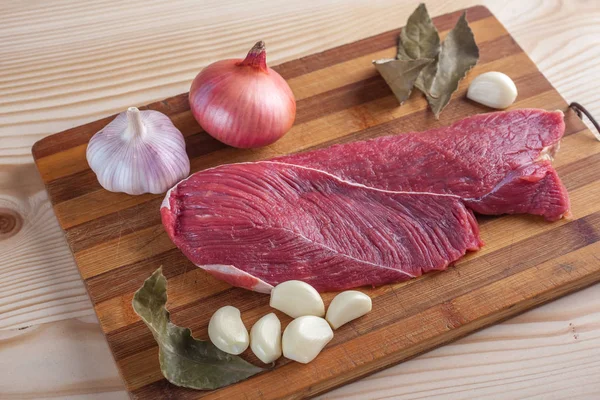 Et, defne yaprağı, sarımsak ve soğan bir kesme tahtası üzerinde