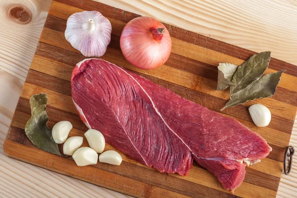 Et, defne yaprağı, sarımsak ve soğan bir kesme tahtası üzerinde