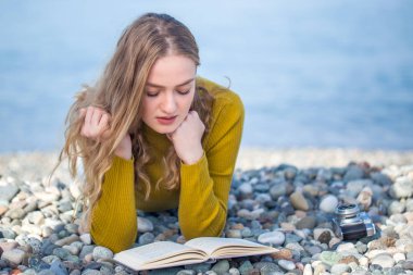 güzel sarışın kız sahilde bir kitap okuyor