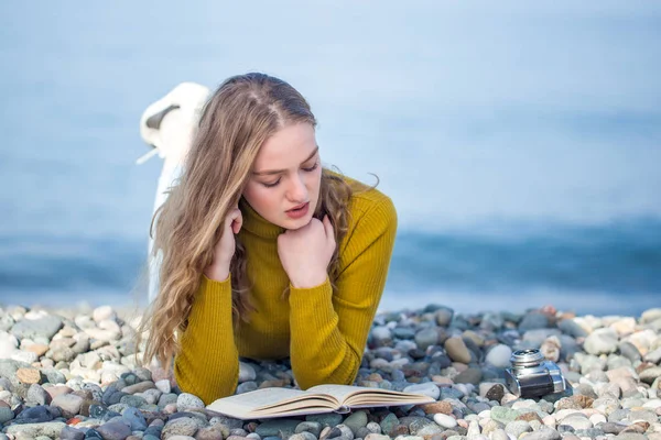 Linda menina loira está lendo um livro na praia — Fotografia de Stock