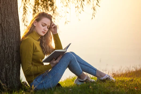 Linda jovem loira sentada e lendo livro em um parque — Fotografia de Stock
