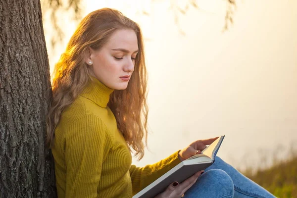 Linda jovem loira sentada e lendo livro em um parque — Fotografia de Stock