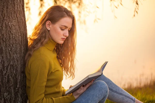 Linda jovem loira sentada e lendo livro em um parque — Fotografia de Stock