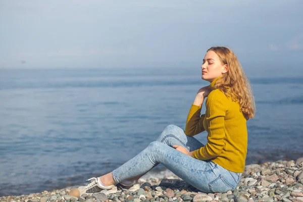 Linda menina loira está sentada na praia e olhando para o — Fotografia de Stock