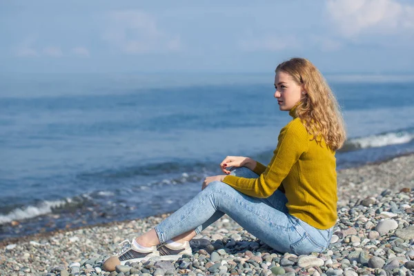 Vacker blond flicka sitter på stranden och tittar på den — Stockfoto