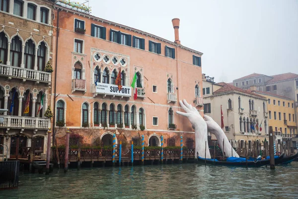 Giant hands rise from the water of the Grand Canal to support th