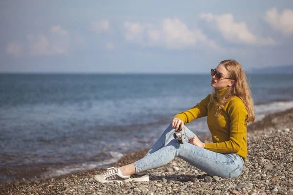 Hermosa chica rubia en una playa de mar con una vieja cámara en la mano — Foto de Stock