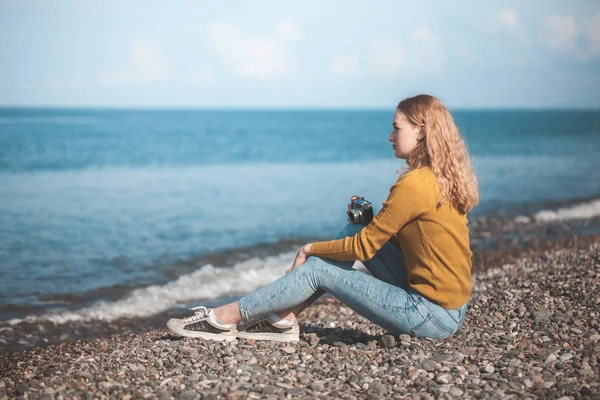 Bella ragazza bionda su una spiaggia di mare con una vecchia macchina fotografica in mano — Foto Stock