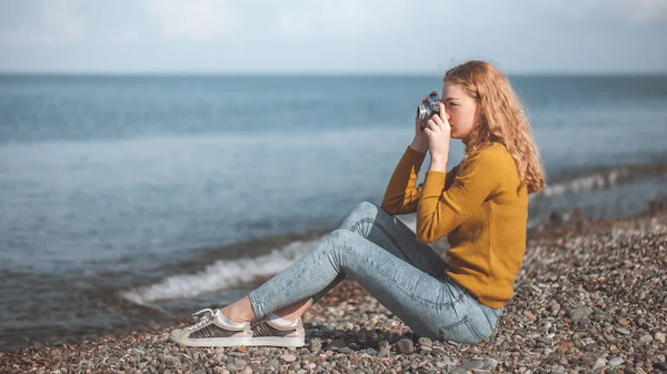 Linda menina loira em uma praia do mar com uma câmera velha na mão — Fotografia de Stock