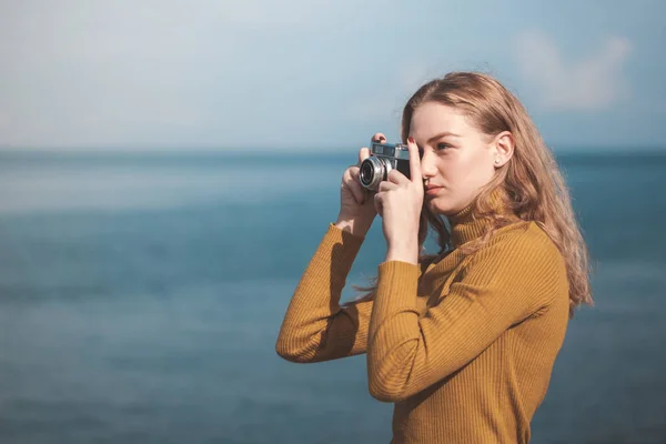 Linda menina loira em uma praia do mar com uma câmera velha na mão — Fotografia de Stock