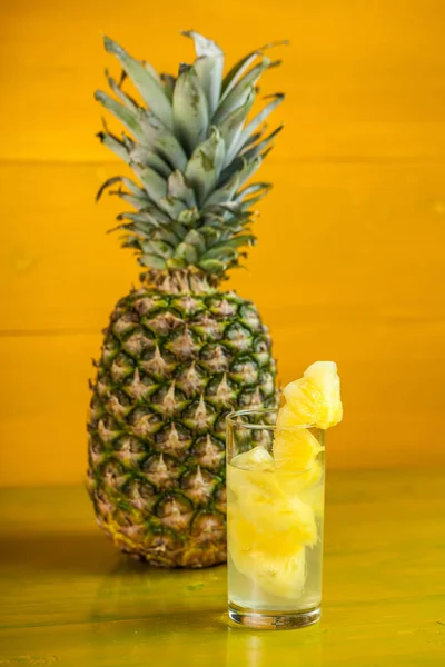 Modne ananas og juice i et glas på en gul træ backgroun - Stock-foto