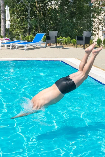 Молодой человек прыгает в бассейн на курорте — стоковое фото