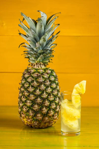 Piña madura y jugo en un vaso sobre un fondo de madera amarilla —  Fotos de Stock