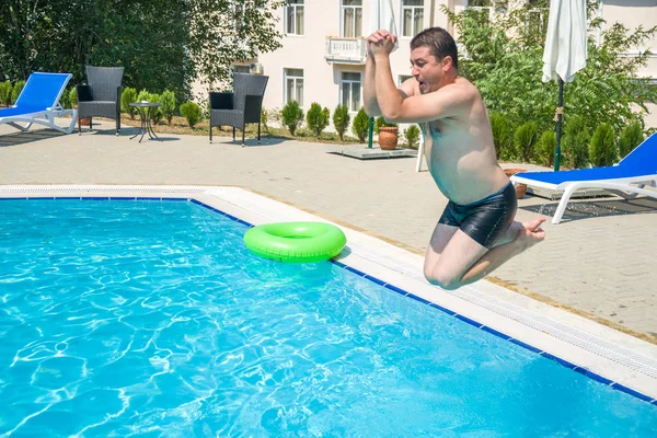 Hombre joven saltando en la piscina en el complejo — Foto de Stock