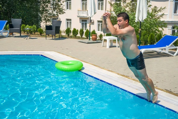 Hombre joven saltando en la piscina en el complejo — Foto de Stock