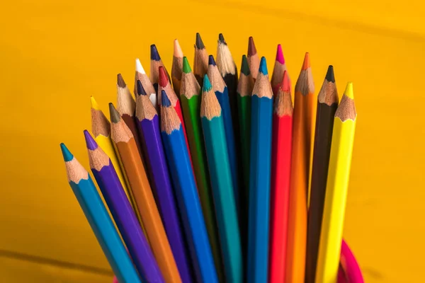 Lápices de color en contenedor de rejilla metálica en el tablero amarillo — Foto de Stock