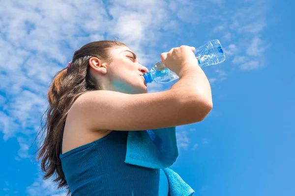 Beautifull girl runner is having break, drinking water against c — Stock Photo, Image