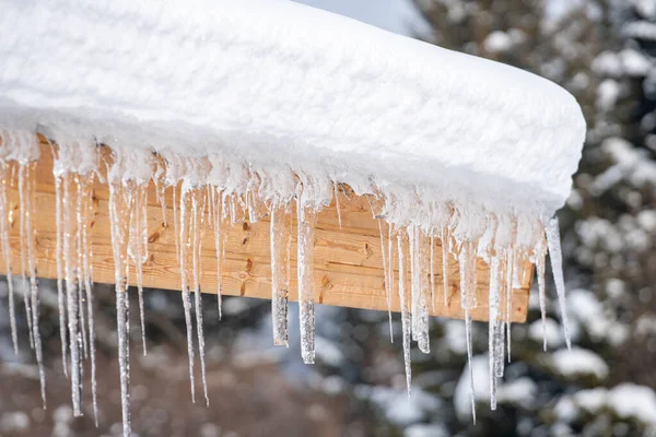 Icicles hang from the snowy roof of a mountain cottage — Stock fotografie