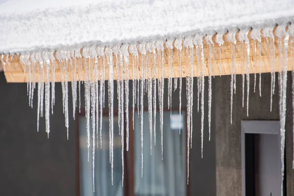 Icicles hang from the snowy roof of a mountain cottage 图库图片