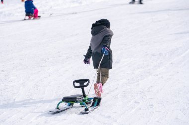 Kayak merkezinde zaman geçirirken kızak çeken ve karlı yamaçlarda koşan çocuğun arka görünümü