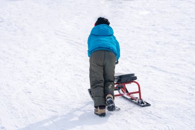 Kayak merkezinde zaman geçirirken kızak çeken ve karlı yamaçlarda koşan çocuğun arka görünümü